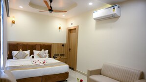 A hotel room with a bed, bedside tables, a sofa, a coffee table, a ceiling fan, and an air conditioning unit. - Hotel Om Villa (Varanasi)