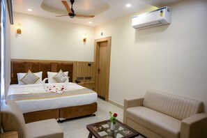 A hotel room with a bed, bedside tables, a sofa, a coffee table, a ceiling fan, and an air conditioning unit. - Hotel Om Villa (Varanasi)