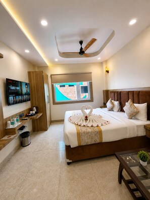 A hotel room with a bed, a TV mounted on the wall, a window, and a ceiling fan. - Hotel Om Villa (Varanasi)