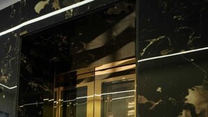 An elevator with a reflective glass door and a control panel with a red light indicator. - Hotel Om Villa (Varanasi)