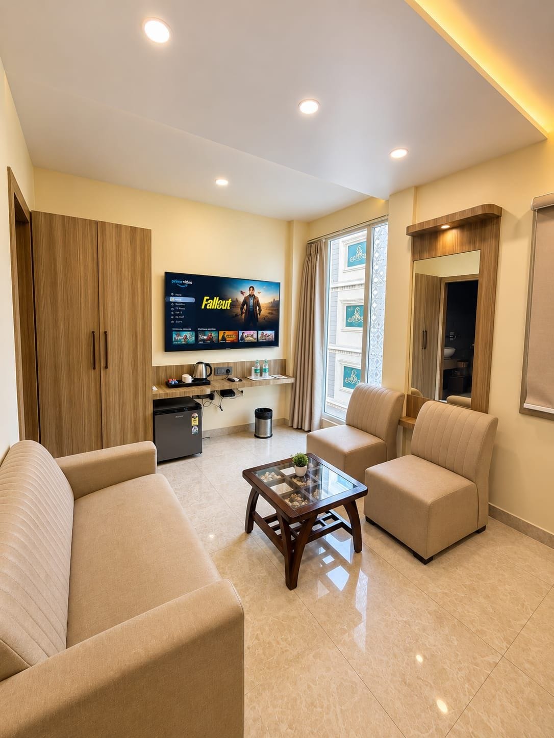 Uma sala de estar moderna com uma TV de tela plana exibindo um filme, uma mesa de centro, dois sofás e uma pequena área de cozinha.