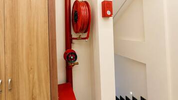 Un pasillo con un armario de madera, una manguera contra incendios roja y una caja de alarmas.