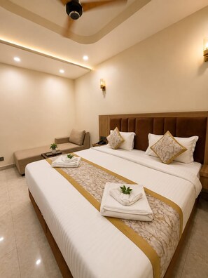 A hotel room with a large bed, a sofa, a bedside table, and a ceiling fan. - Hotel Om Villa (Varanasi)