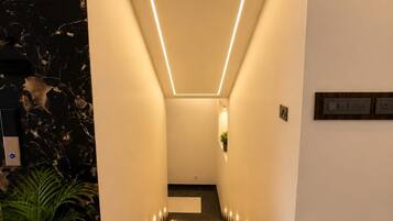 Un pasillo moderno con un aplique geométrico, paredes de mármol y una planta en maceta.
