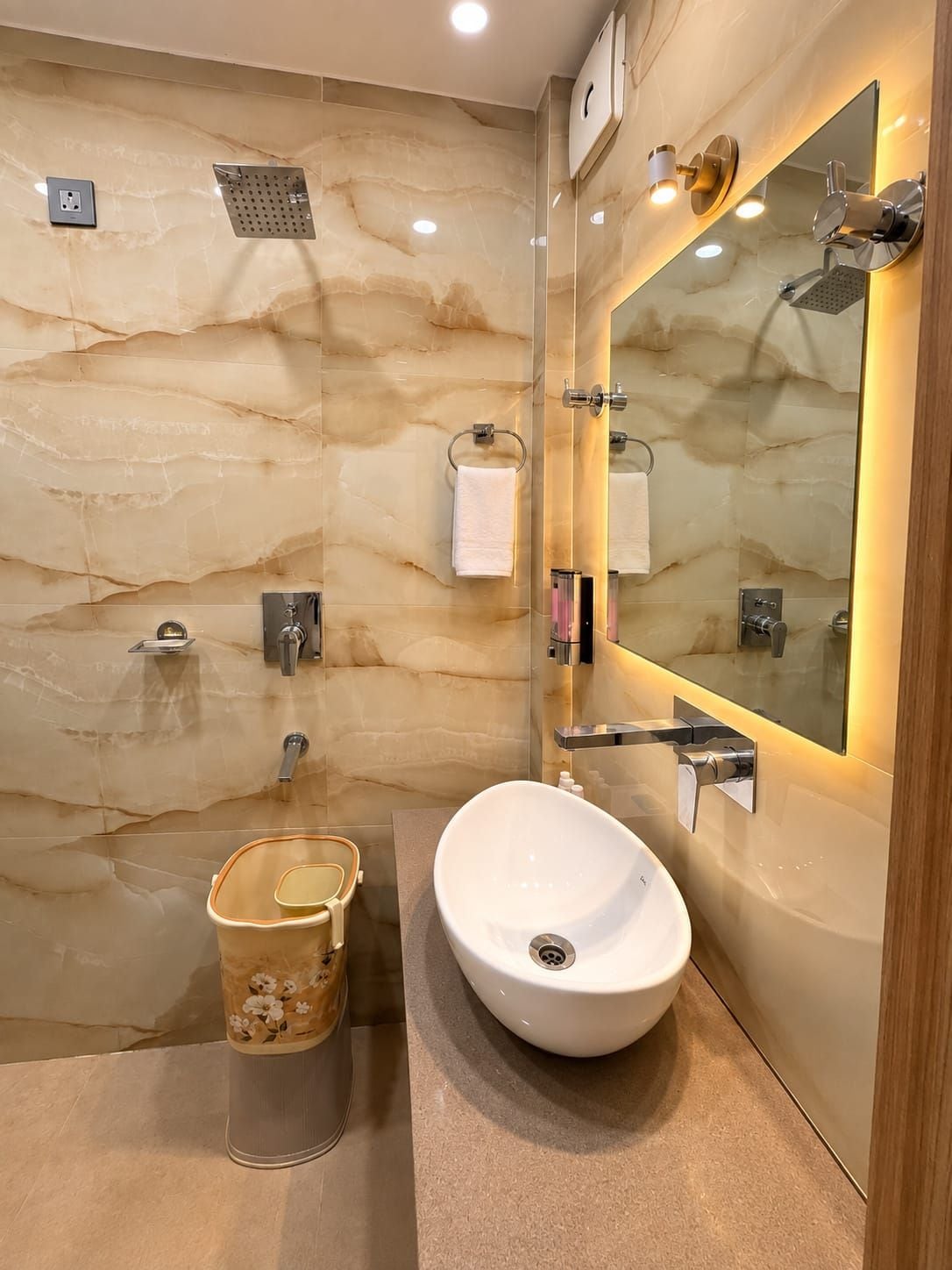 A modern bathroom with a marble wall, a large mirror, a sink, and a shower.