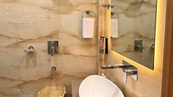 A modern bathroom with a marble wall, a large mirror, a sink, and a shower.