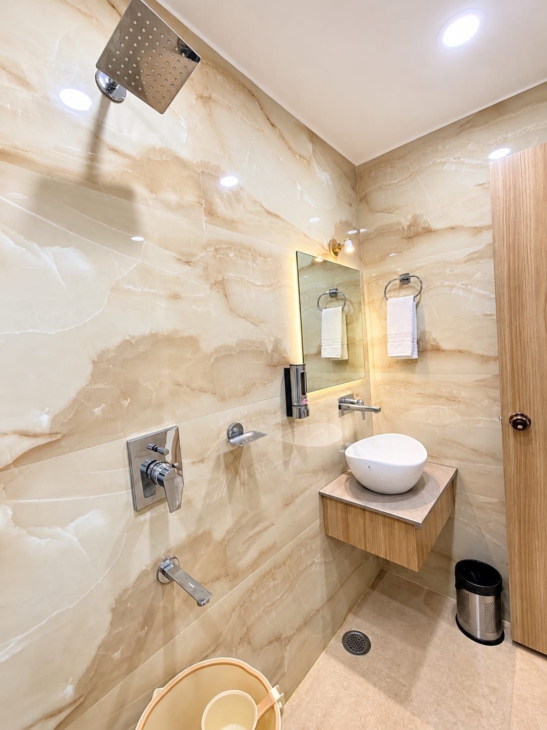 A modern bathroom with a marble wall, a sink, a mirror, a towel rack, and a showerhead.