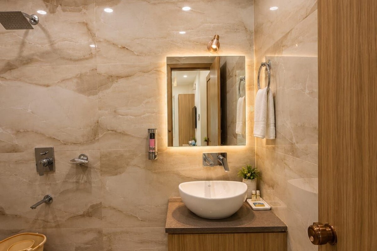 A modern bathroom with a marble wall, a wooden vanity, a large mirror, a shower, and a toilet.