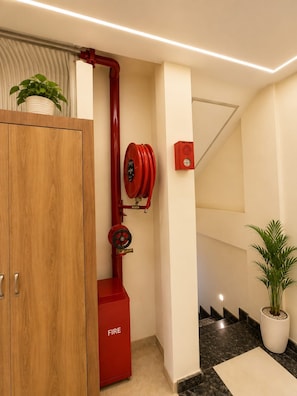 A hallway with a wooden cabinet, a red fire hose reel, and a fire alarm box.
