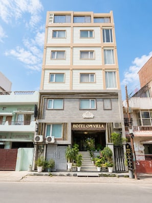 A multi-story hotel with a prominent entrance, air conditioning units, and potted plants.
