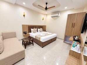 A hotel room with a bed, a sofa, a small table, an air conditioning unit, a television, and a kitchenette. - Hotel Om Villa (Varanasi)