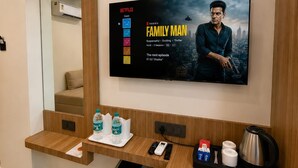 A hotel room with a mounted television displaying a Netflix series, a wooden console with amenities, and a mirror. - Hotel Om Villa (Varanasi)