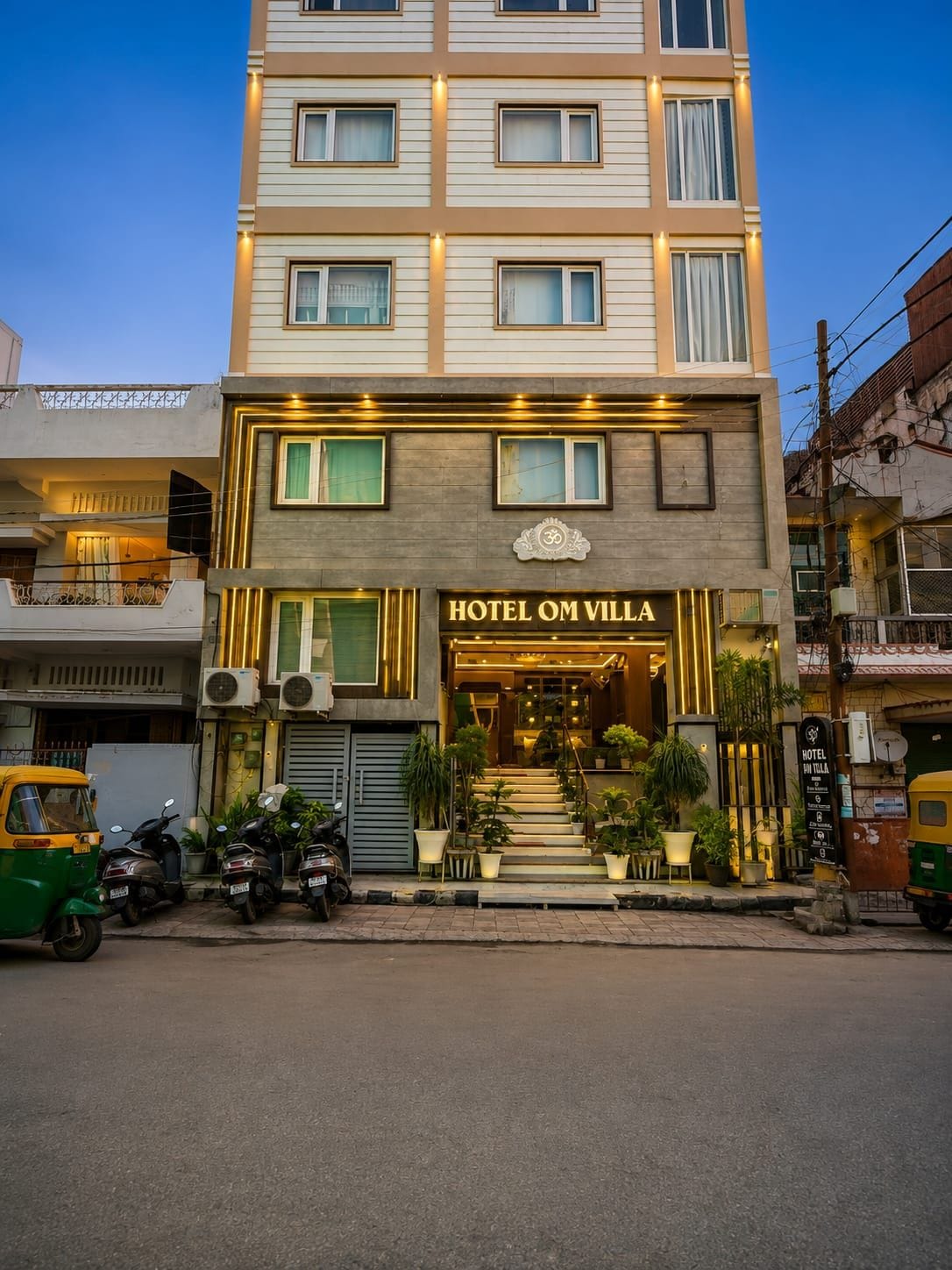 Um hotel com vários andares, uma entrada notável e uma escadaria que leva à entrada, com uma placa que diz 'HOTEL OM VILLA'.
