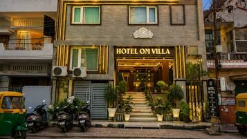 Um hotel com vários andares, uma entrada notável e uma escadaria que leva à entrada, com uma placa que diz 'HOTEL OM VILLA'.