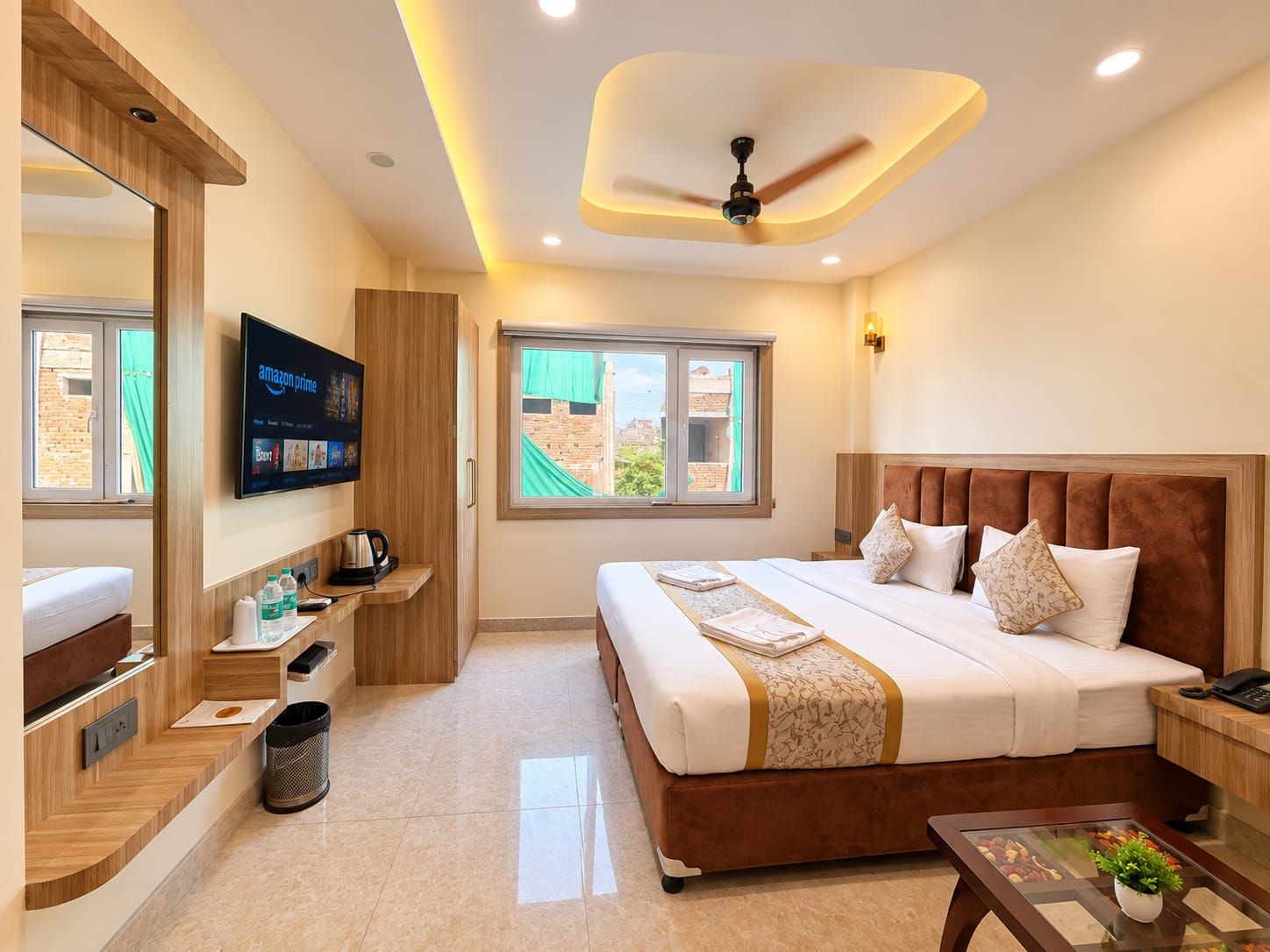 Habitación de hotel con cama, televisor, ventana, ventilador de techo y una mesita con una planta.