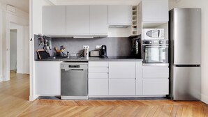 A modern kitchen with white cabinets, a stainless steel refrigerator, a built-in oven, and a dishwasher.