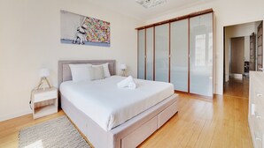 Een slaapkamer met een bed, nachtkastjes, een schilderij, een kledingkast en uitzicht op de gang.