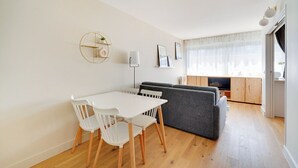 A modern living room with a dining area, featuring a sofa, a TV, and a dining table with chairs.