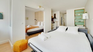 A modern hotel room with a large bed, a small sofa, a wooden floor, and a kitchenette.