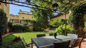 An outdoor patio with a table and chairs, surrounded by greenery and a view of buildings.