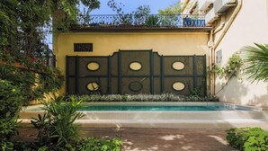 A pool area with a wooden deck, surrounded by lush greenery and a decorative wall with circular cutouts.