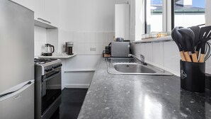 A modern kitchen with white cabinetry, a stainless steel stove, a sink, and a window with a view of a building. - Charming London Apartment Near City Center (London)