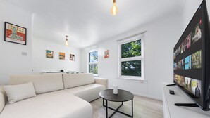 A modern living room with a sectional sofa, a coffee table, and a flat-screen TV mounted on the wall. - Charming London Apartment Near City Center (London)