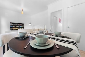 Un coin repas avec une table ronde dressée pour quatre personnes, agrémentée de bols et d’assiettes bleu clair, d’un chemin de table à rayures et d’un luminaire suspendu moderne.
