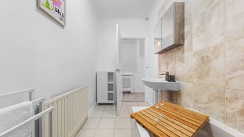 A narrow hallway with a white radiator, a wooden bench, a white sink, and a door leading to another room.