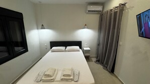 Habitación de hotel con cama, dos lámparas de noche, aire acondicionado, ventana y televisor en la pared.