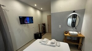 Una habitación de hotel con una cama, un televisor montado en la pared, una tocador de madera con espejo y un altavoz negro pequeño.