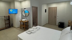 A hotel room with a bed, a wooden side table with a sink, a mirror, a TV, and a wardrobe. - Georgias House Project North (Skiathos)