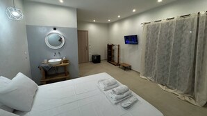 A hotel room with a bed, a round mirror, a sink, a television, and a shower curtain. - Georgias House Project North (Skiathos)