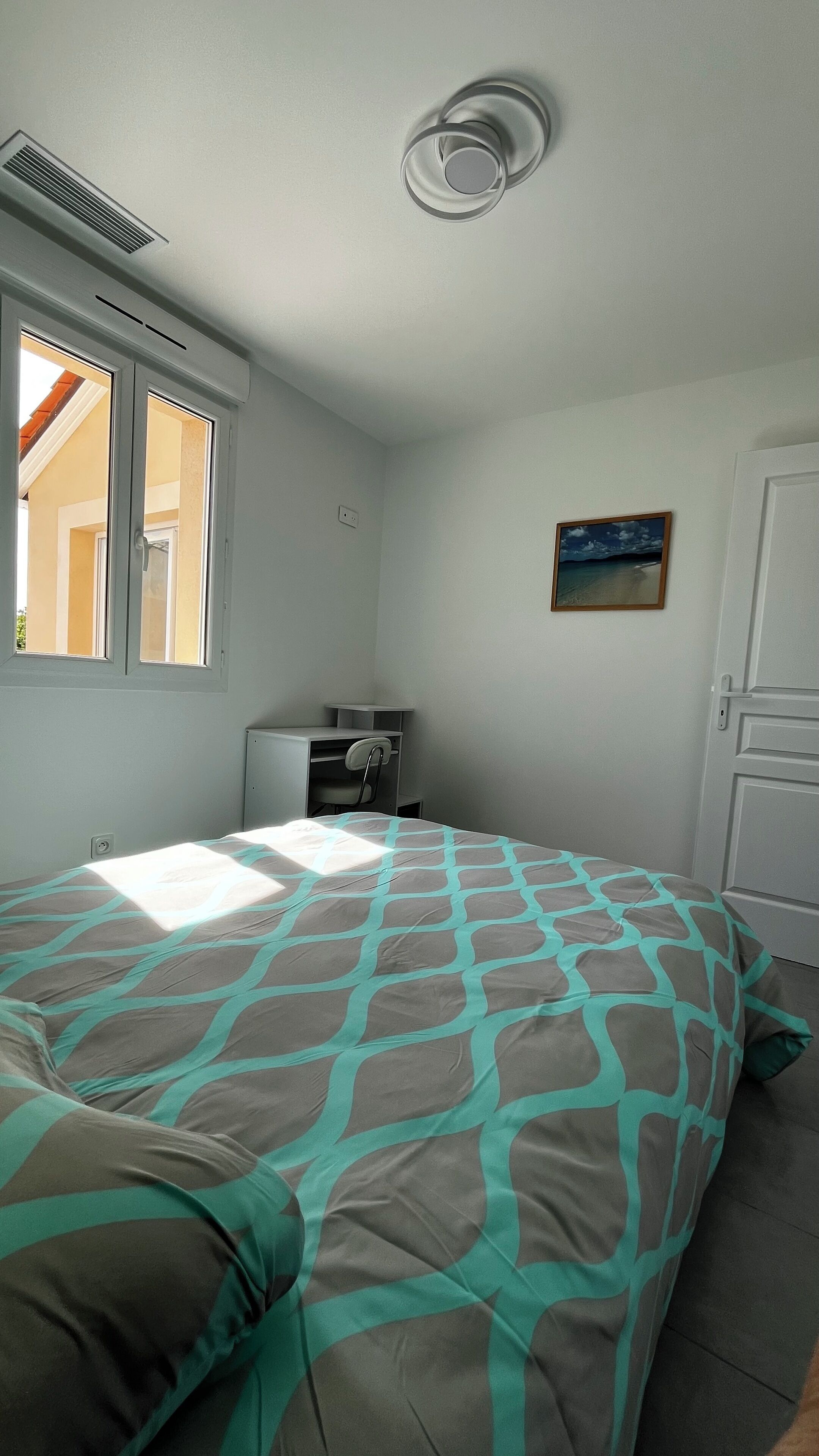 A bedroom with a bed, a desk, a chair, a radiator, a window, and a door.