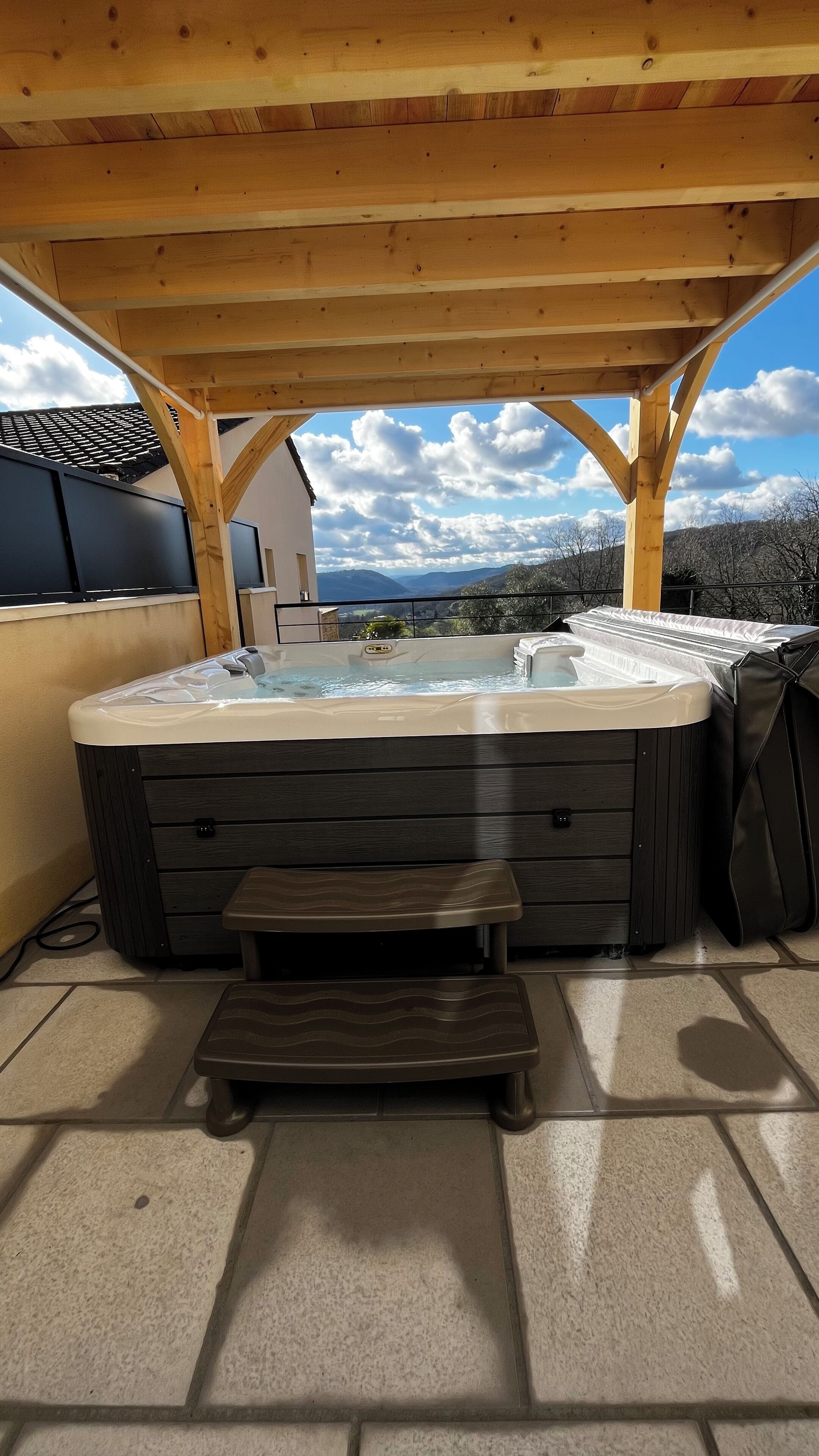 Un bain à remous sous une pergola en bois, avec vue sur les montagnes.