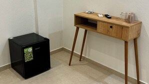 A small black refrigerator with an energy efficiency sticker, a wooden desk with a drawer, and a few items on top including a remote control and jars. - Georgias House Project West (Skiathos)