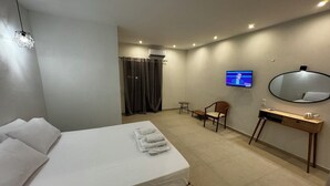 A modern hotel room with a large bed, a desk with a mirror, a TV, and a small chair. - Georgias House Project West (Skiathos)