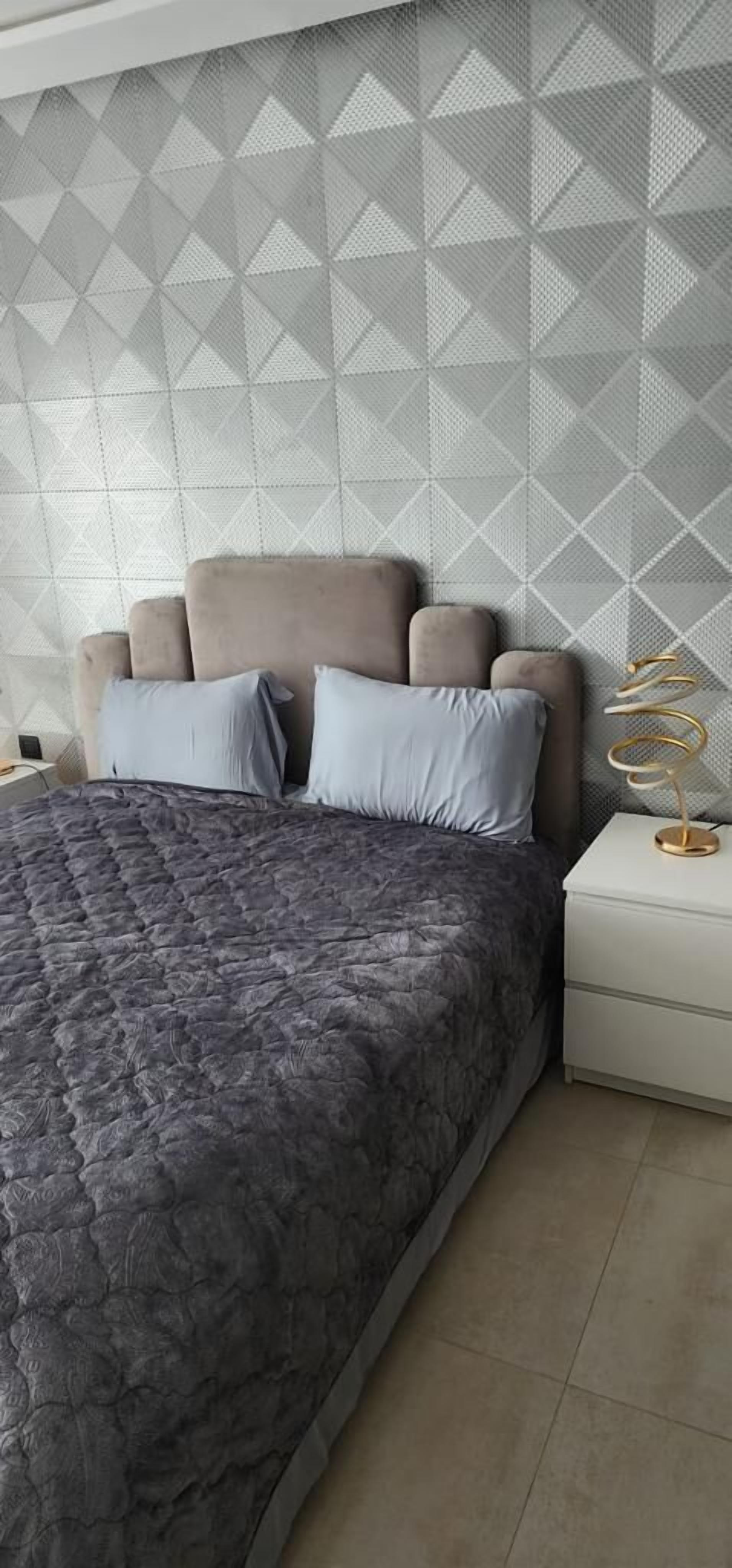 Un dormitorio con cama, mesita de noche y pared con diseño geométrico.