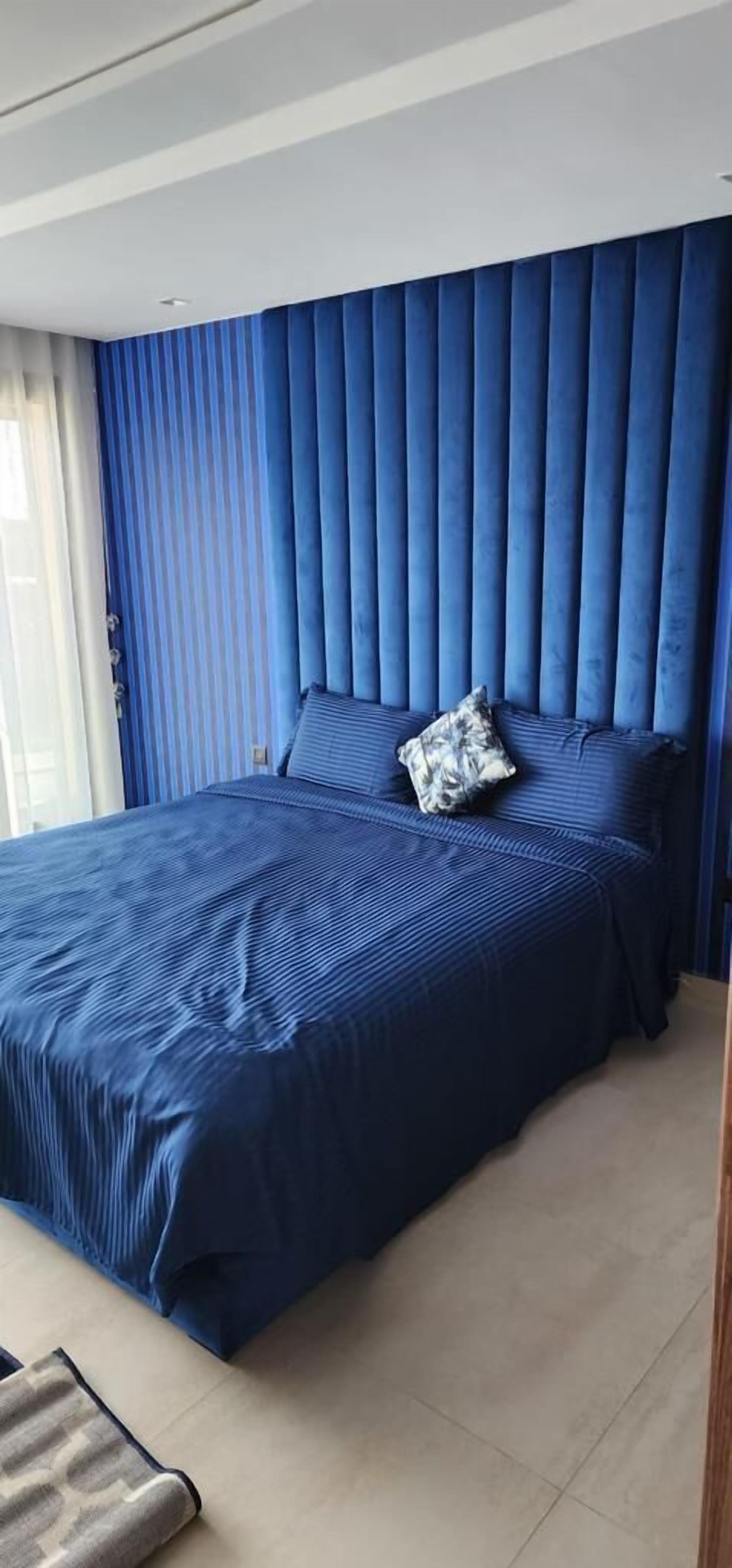 Un dormitorio con una cama grande, cortinas azules y un almohadón a rayas.
