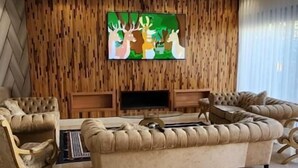 Een moderne woonkamer met een ruime beige bank, een flatscreen televisie aan een houten wand en een open haard.