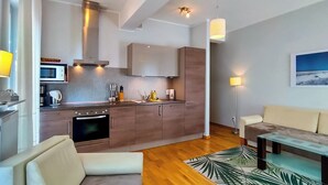 A modern kitchen with built-in appliances, a dining area with a glass table, and a living room with a sofa and a painting on the wall.