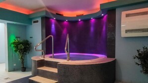 A spa area with a hot tub, steps leading up to it, and a wall with a water feature.