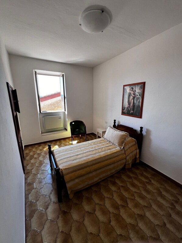 Ein Schlafzimmer mit einem Bett, einem Sessel, einem Fenster und einem Bild an der Wand.