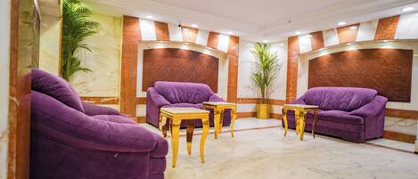 A lobby with purple sofas, wooden tables, and a marble floor.