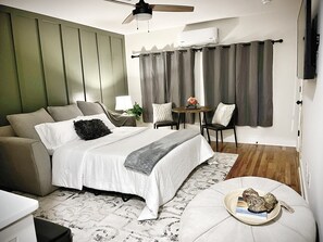 Ein modernes Schlafzimmer mit einem Bett, einer Sitzecke und einem kleinen Tisch mit einer Lampe.