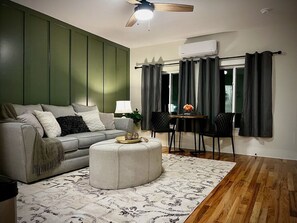 Ein Wohnzimmer mit einer Couch, einem Hocker und einem Essbereich mit Tisch und Stühlen.