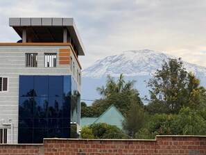 A modern building with a flat roof and large windows, set against a backdrop of a snow-capped mountain. - Kilimanjaro Home Of Travelers (Moshi)