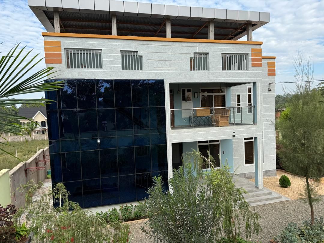 Una casa moderna de dos pisos con fachada de vidrio, un balcón y un pequeño jardín.
