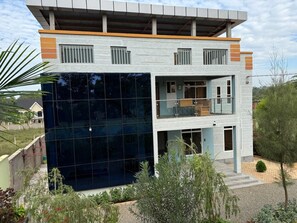 A modern two-story house with a glass facade, a balcony, and a small garden area. - Kilimanjaro Home Of Travelers (Moshi)