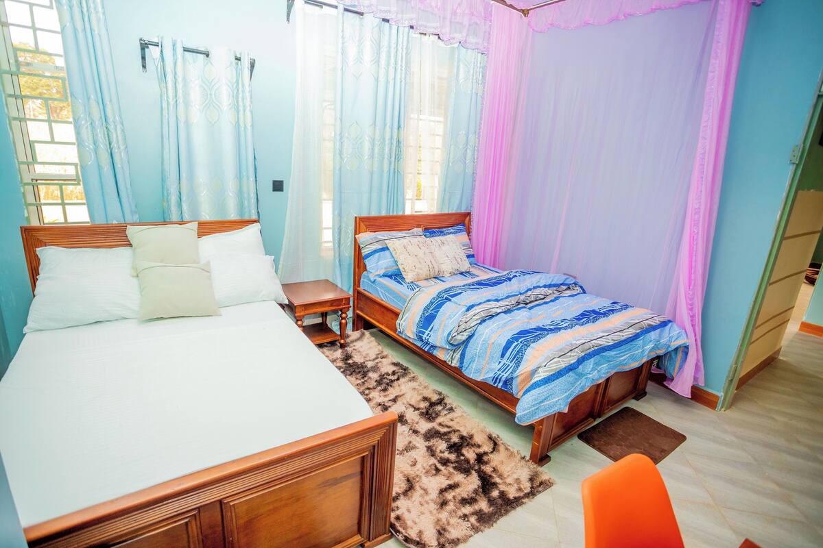 A bedroom with two beds, a wooden headboard, a nightstand, a fluffy rug, and a window with curtains.